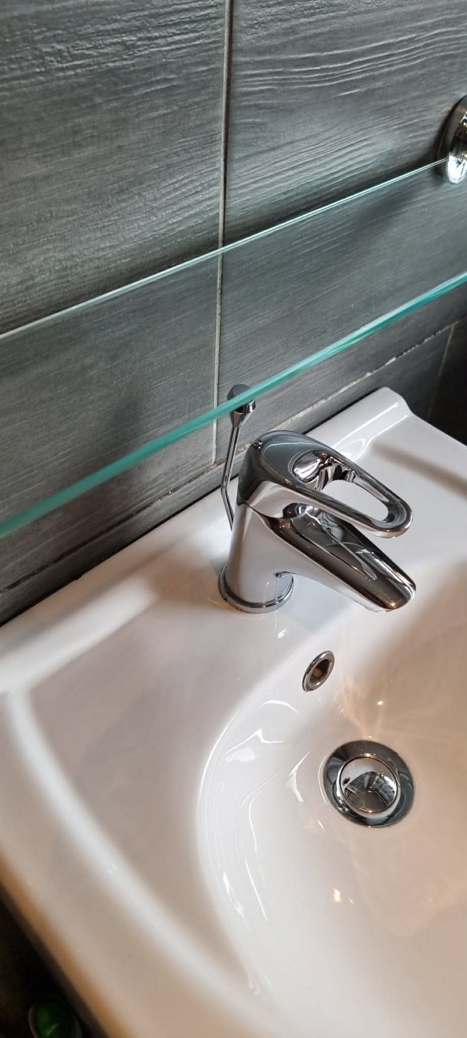 Bathroom basin, polished tap and clear glass shelf after cleaning
